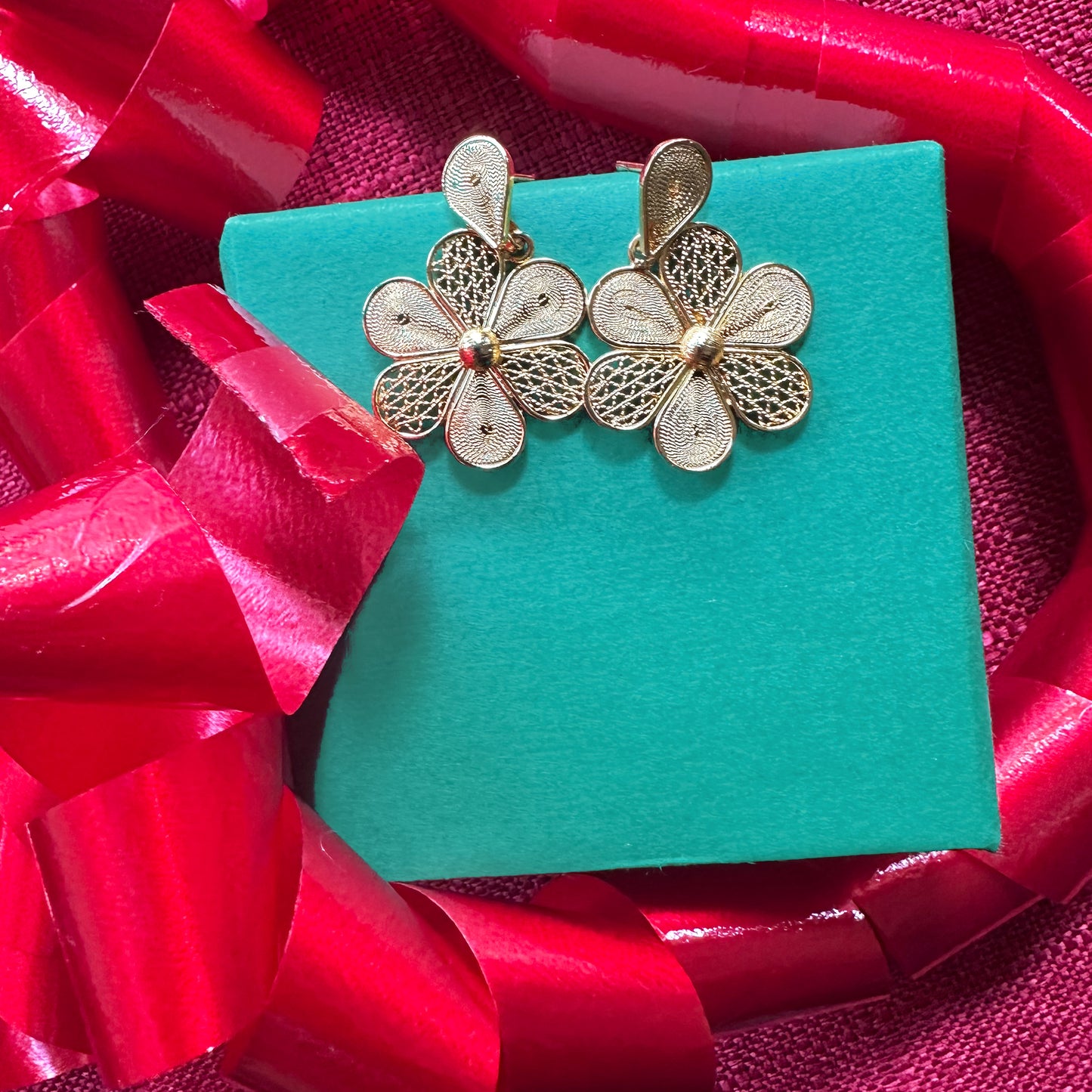Con Cariño Earrings - Gold floral filigree earrings with petal-shaped detailing displayed on a teal gift box, surrounded by vibrant red ribbon, perfect for a festive or holiday-themed jewelry presentation.