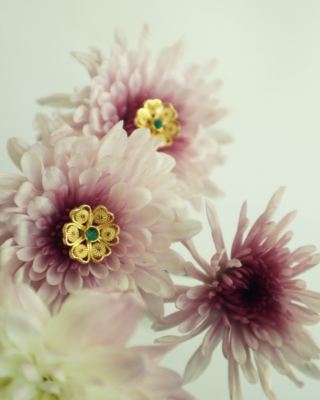 Con Cariño Earrings - Gold floral filigree stud earrings with green center stones placed at the heart of soft pink chrysanthemum blooms, blending handcrafted elegance with natural beauty.