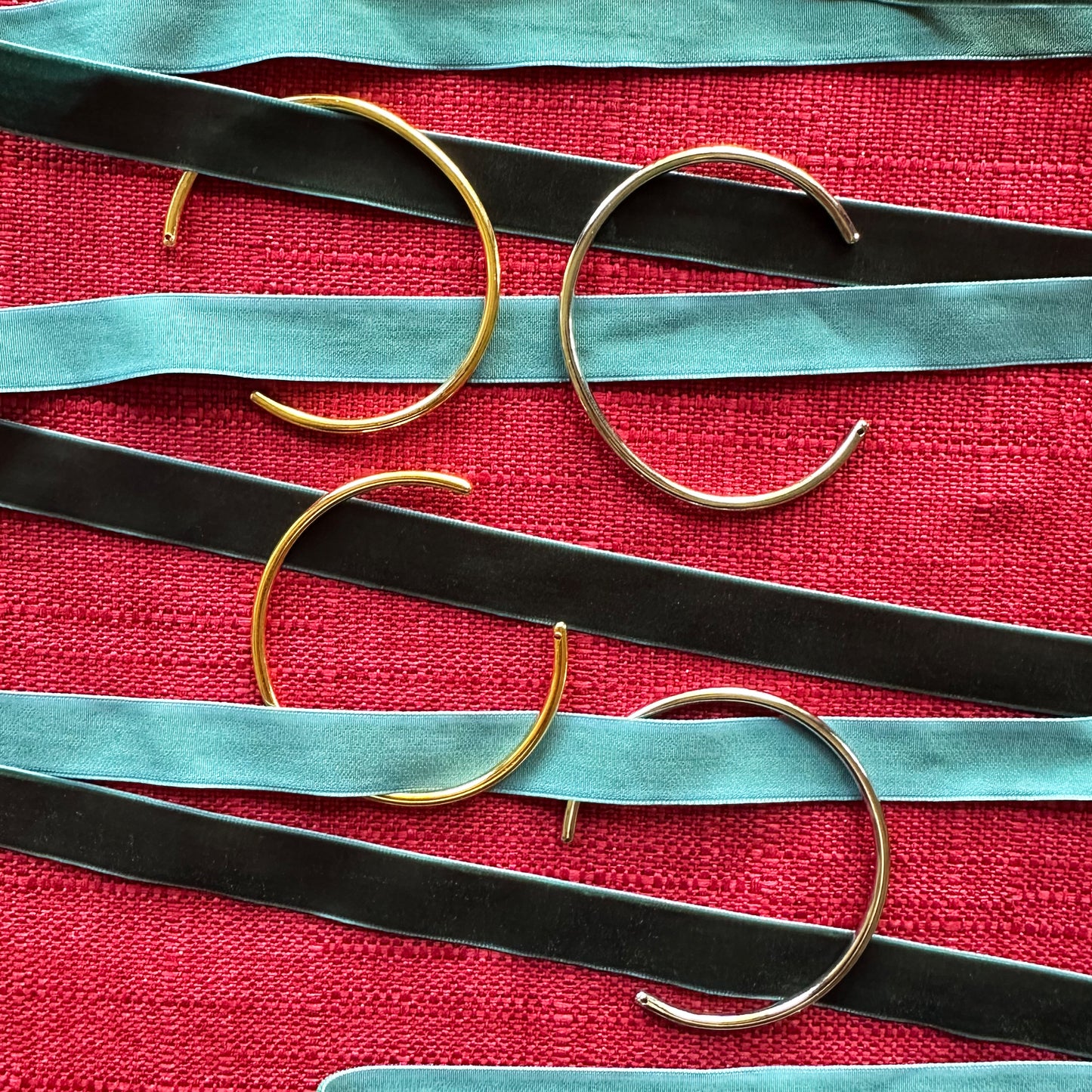 Con Cariño Earrings - Set of sleek, minimalist gold bangles placed styled on a rich red textured fabric for a festive presentation.