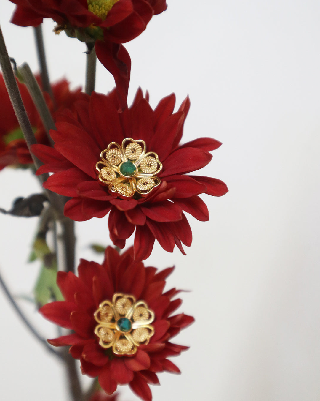 Con Cariño Earrings - Gold floral filigree stud earrings with green center stones nestled in deep red chrysanthemum flowers, emphasizing artisanal detail and rich contrast.
