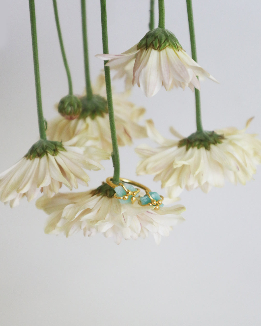 Gold ring with raw emerald stones, handmade in Colombia. Styled on soft white chrysanthemums. 
