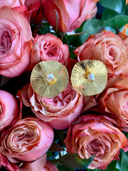 Con Cariño Earrings - Bold gold disc earrings with a radiant textured finish and central pearl accent, beautifully displayed on multi colored roses.