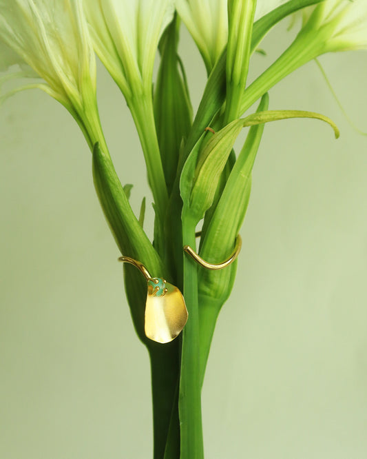 Con Cariño Earrings - Elegant gold cuff bracelet with a petal-shaped detail and raw green stone, displayed on the stem of a white lily flower, blending botanical inspiration with handcrafted sophistication.