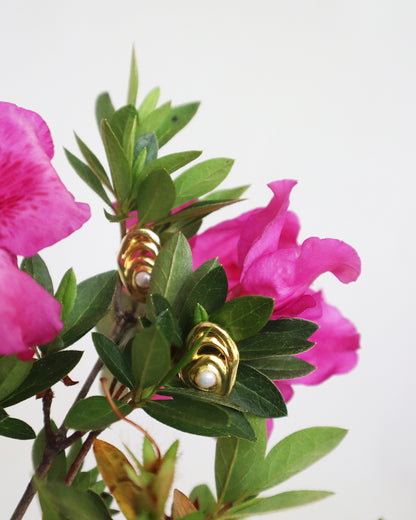 Con Cariño Earrings - Gold abstract pearl earrings nestled among vibrant pink flowers and lush green leaves, showcasing a modern design inspired by organic shapes and natural beauty.