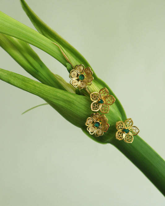 Con Cariño Earrings - Delicate gold flower-shaped stud earrings with filigree detailing and green center stones, artistically arranged on a fresh green lily stem, showcasing handmade Colombian craftsmanship.